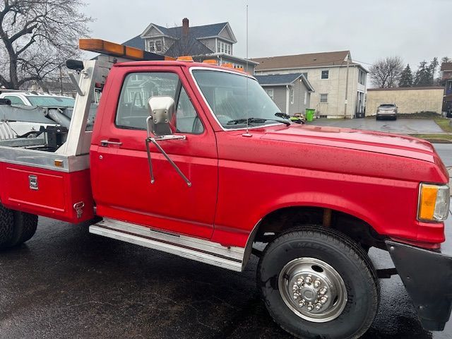 a 1989 Ford F-450  tow truck is parked on the the road