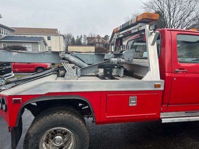 a red  1989 Ford F-450  tow truck is parked on the side of the road