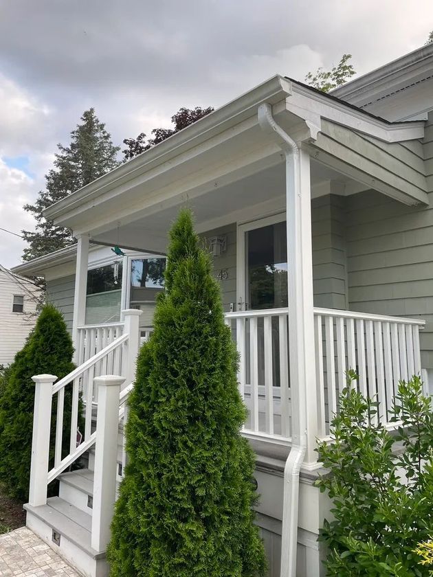 Front porch of a light green house with white railings and a tall shrub in front