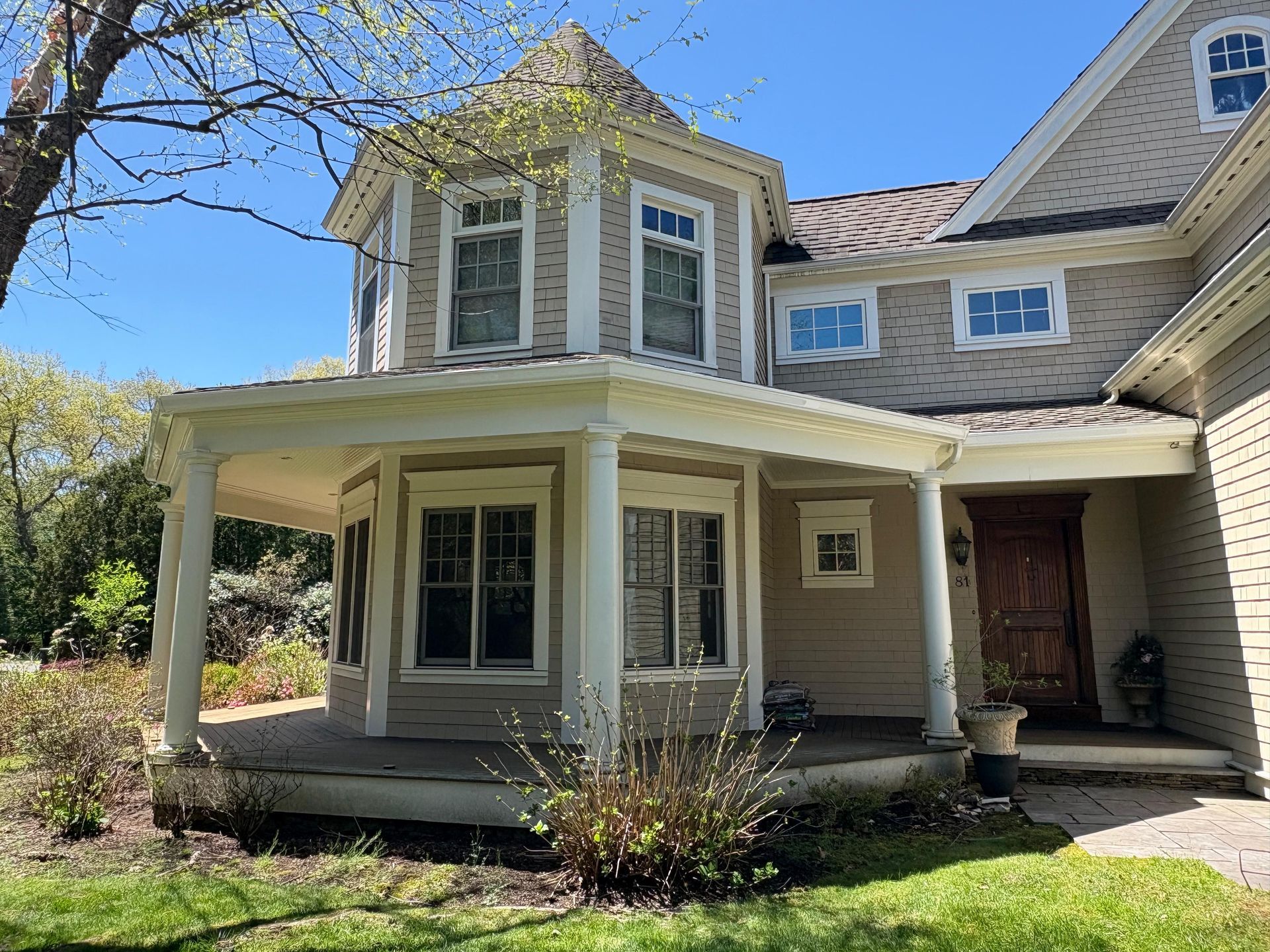 Two-story beige house with white porch and bay windows under a bright blue sky
