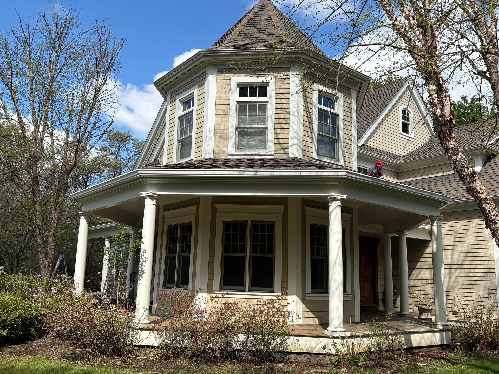 Victorian-style house with a wraparound porch and bay windows, framed by trees under a partly cloudy sky