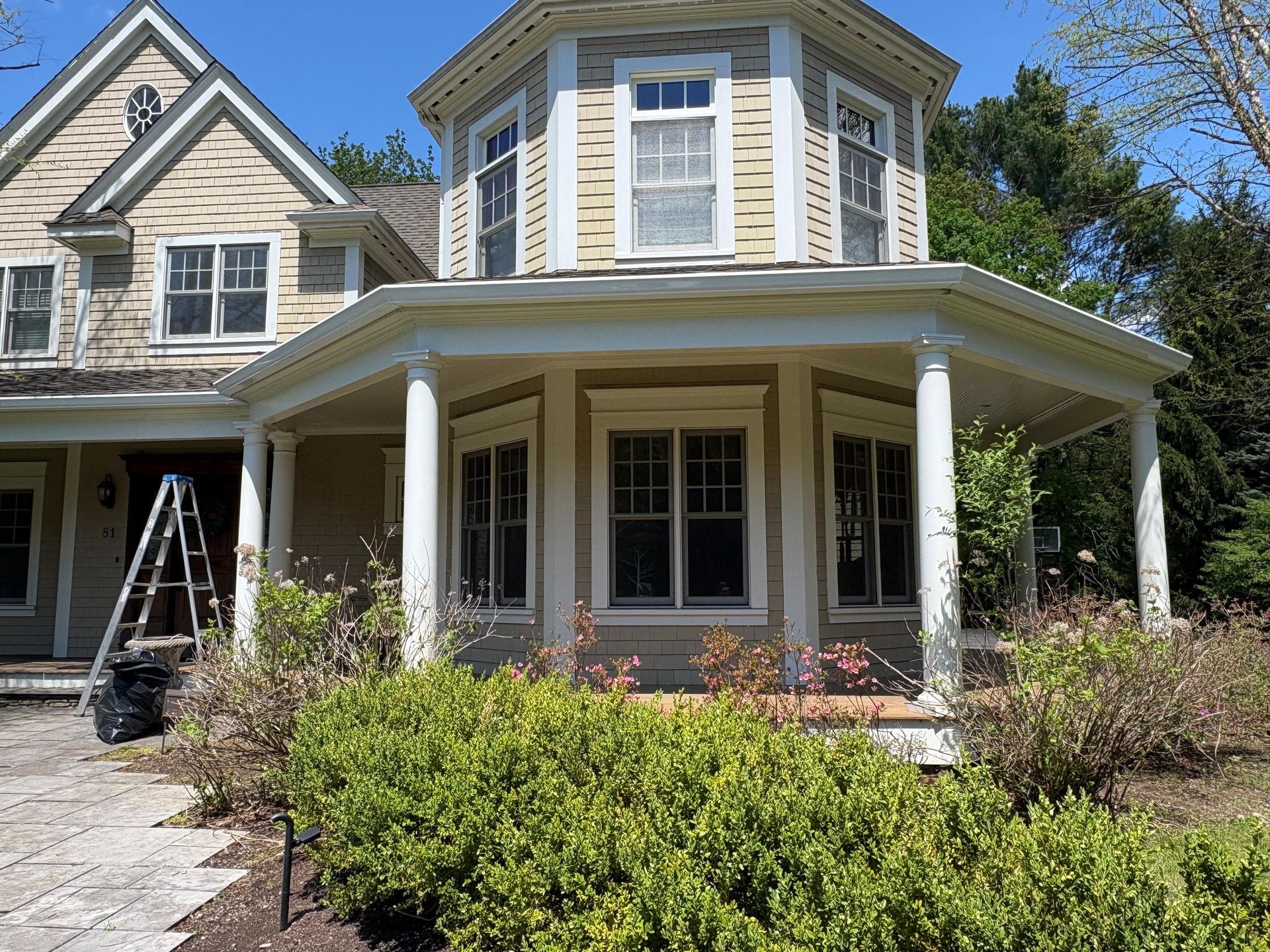 Two-story house with cream trim, wraparound porch, and bay windows, fronted by shrubs and a driveway