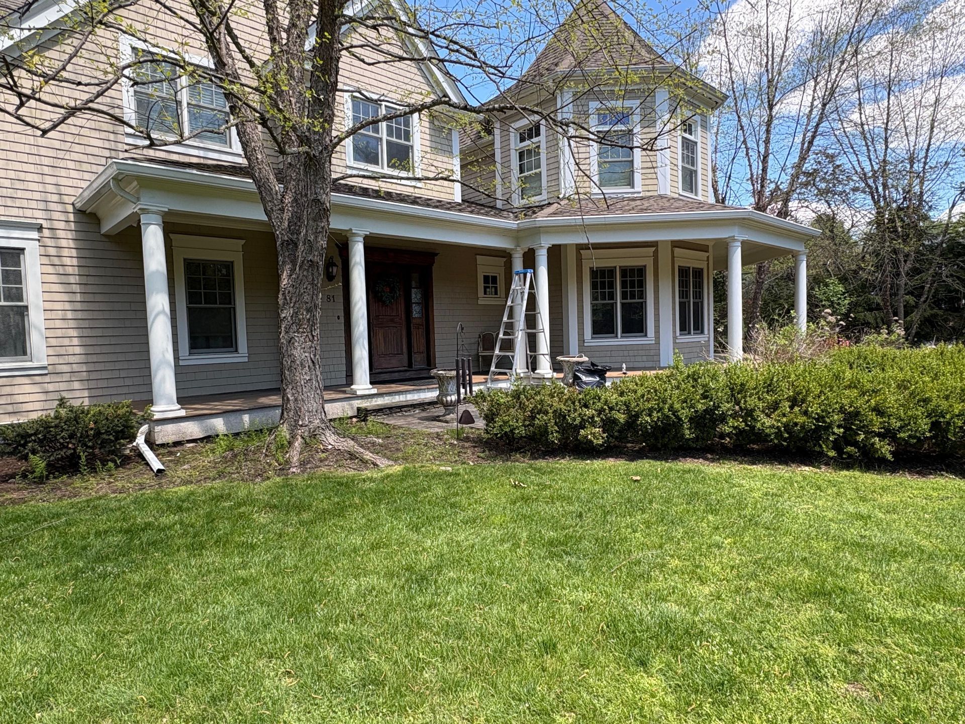 Two-story house with a wraparound porch, white siding, and a green lawn in front