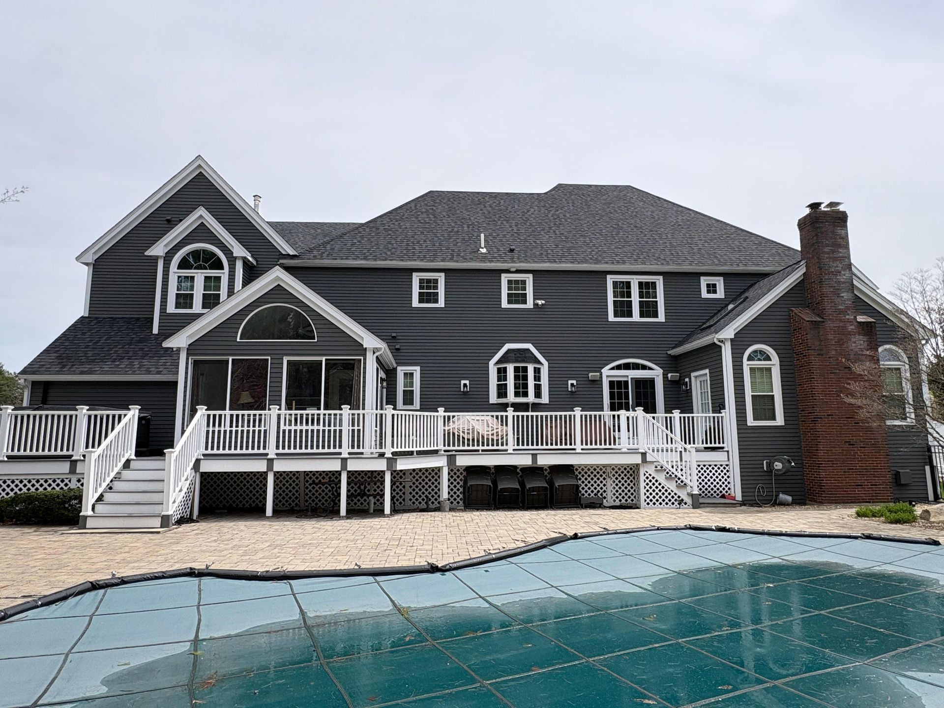Large dark gray house with white trim, porch, and brick chimney beside a swimming pool