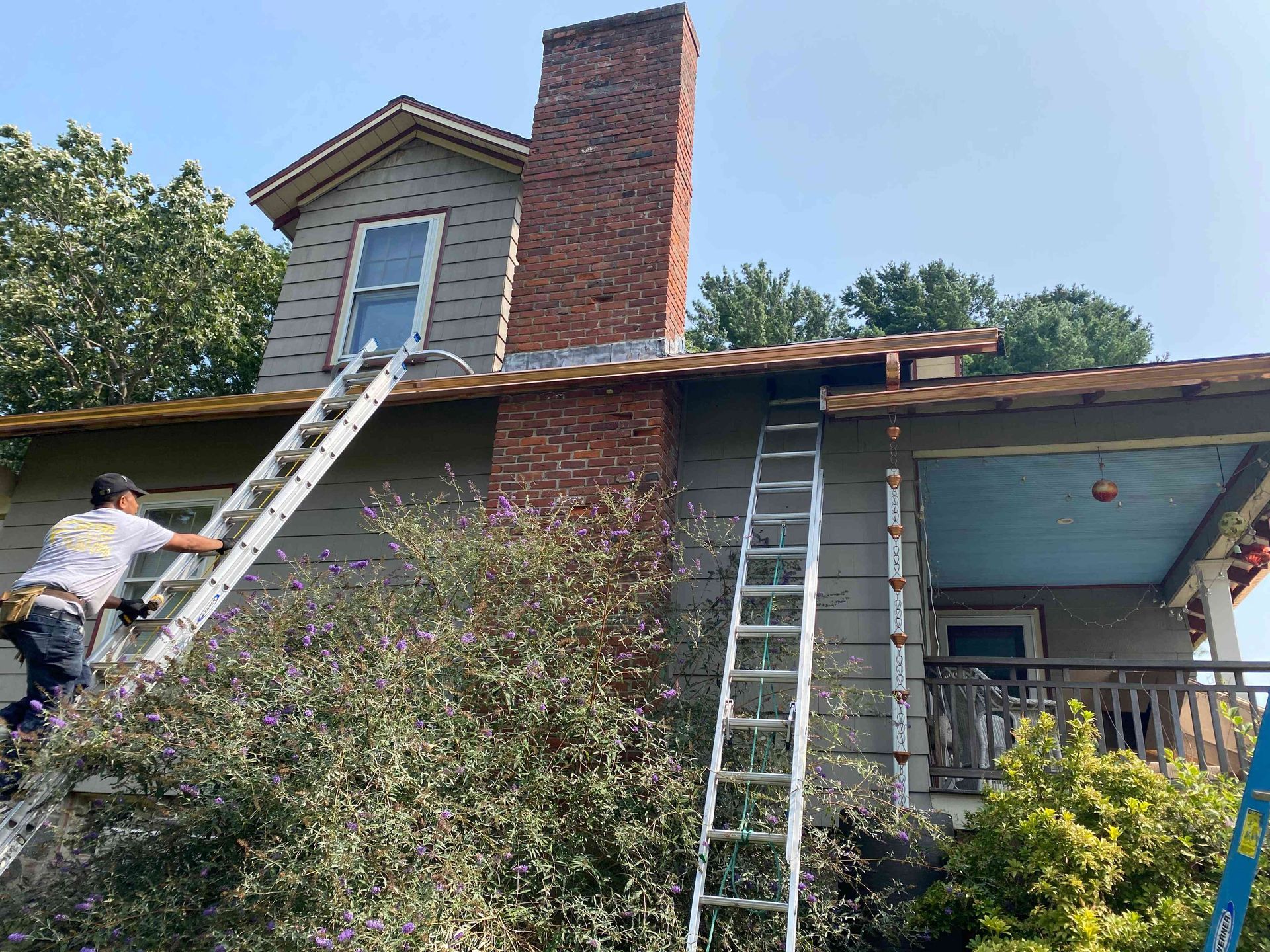 Workers on ladders repairing a house roof and brick chimney
