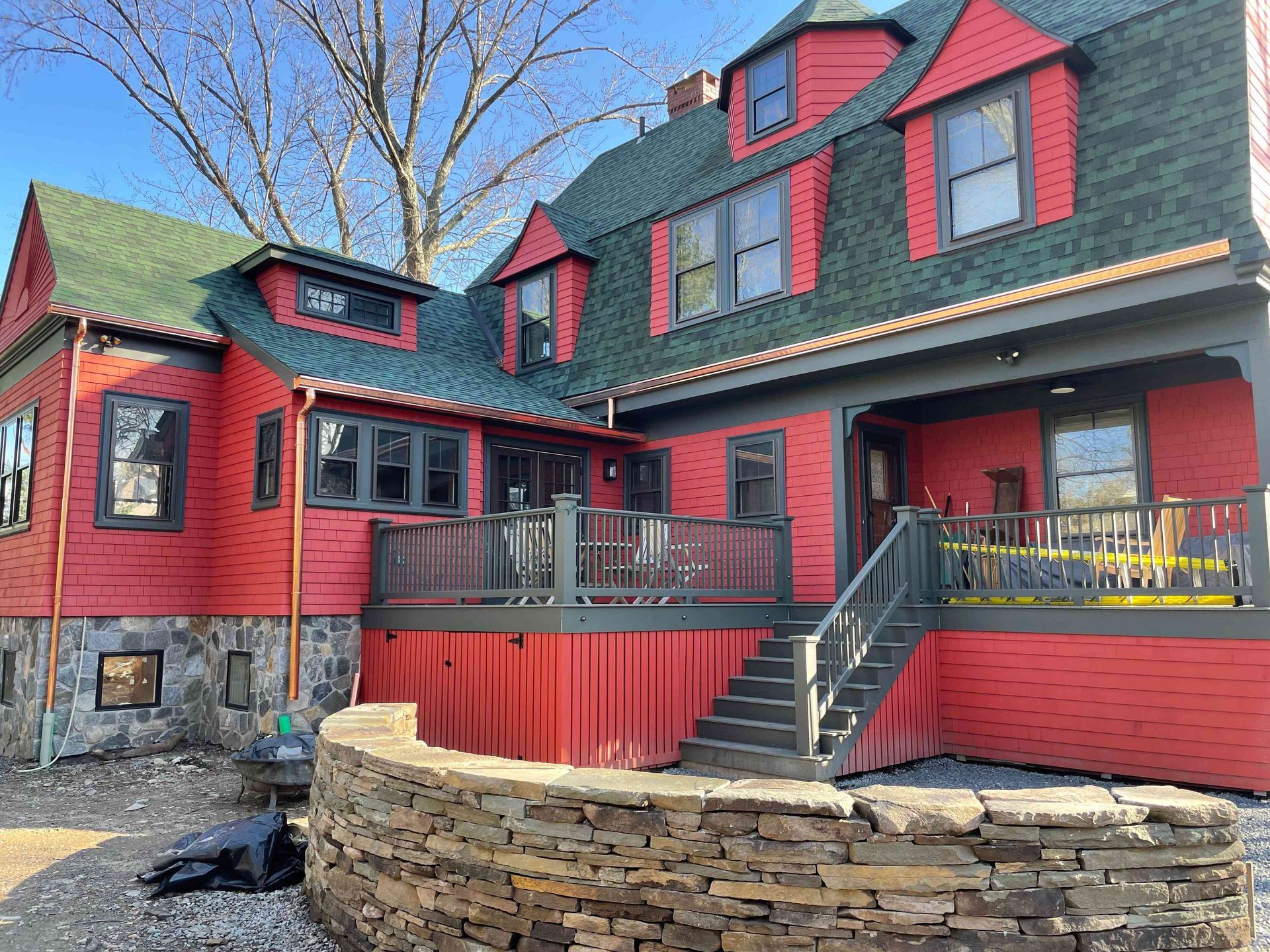 Red Victorian-style house with black roof, red trim, and a stone retaining wall in front