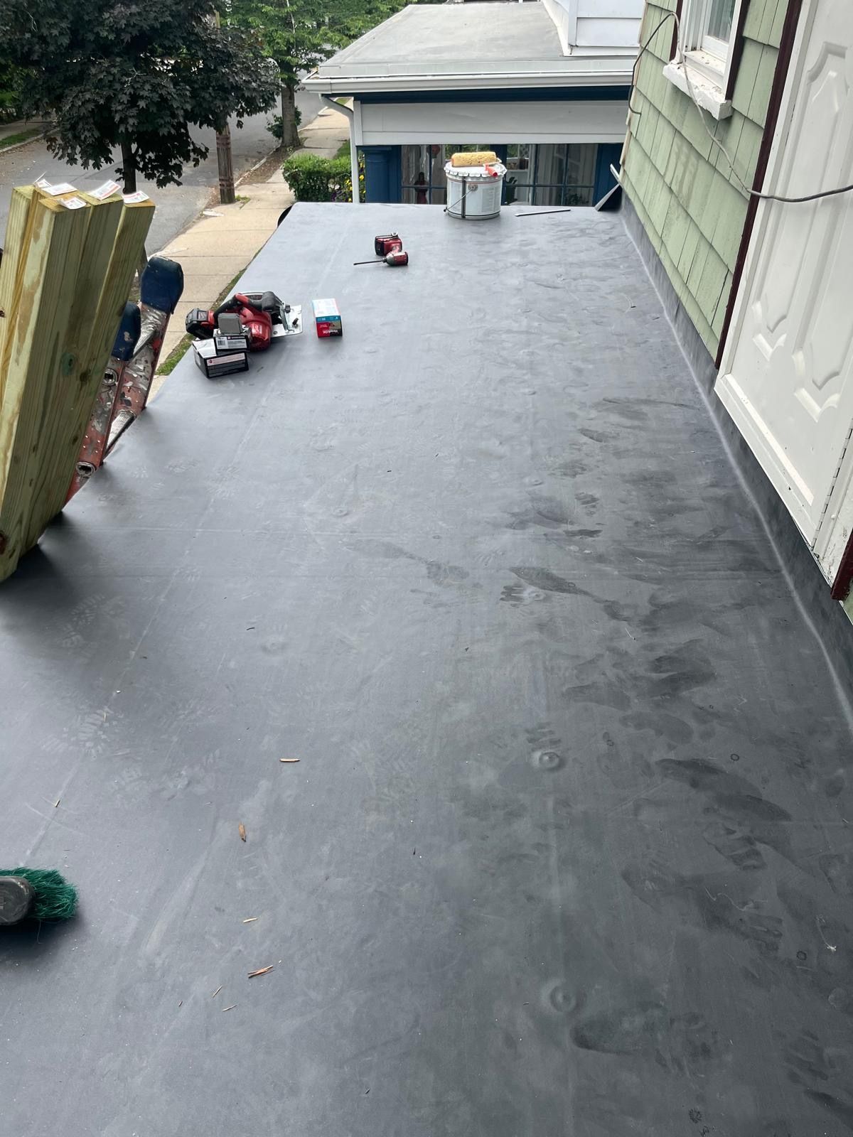 Flat black roof under construction with tools and a bucket near the far end, viewed from above