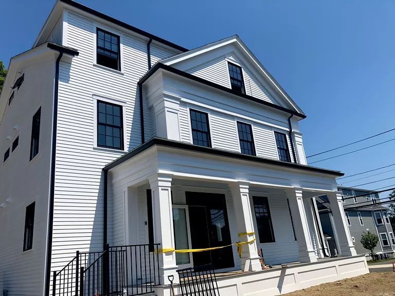 White two-story house with dark shutters, a front porch, and a peaked roof under a clear blue sky