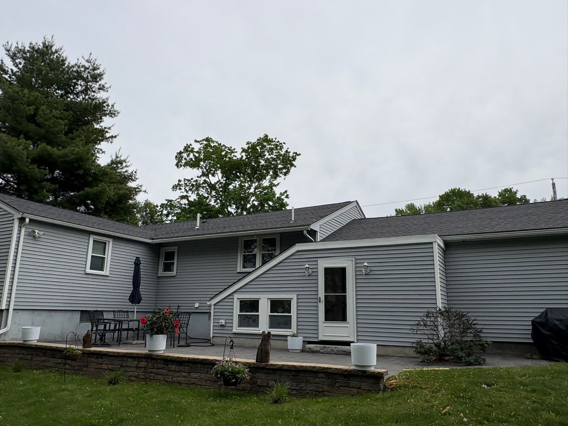 Gray house exterior with white trim, multiple windows, and a small front garden under an overcast sky