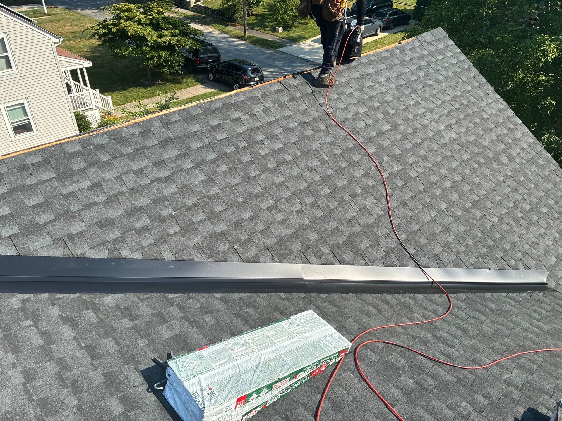 Roofing work with gray shingles, a worker, tools, and a red cord on a residential roof