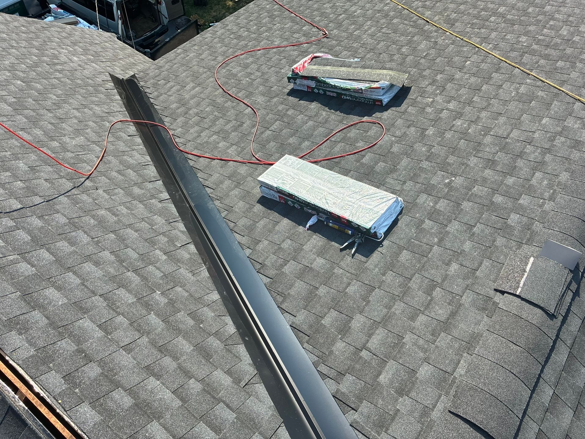 Rooftop with gray shingles, two HVAC units, and red cables near a central seam.
