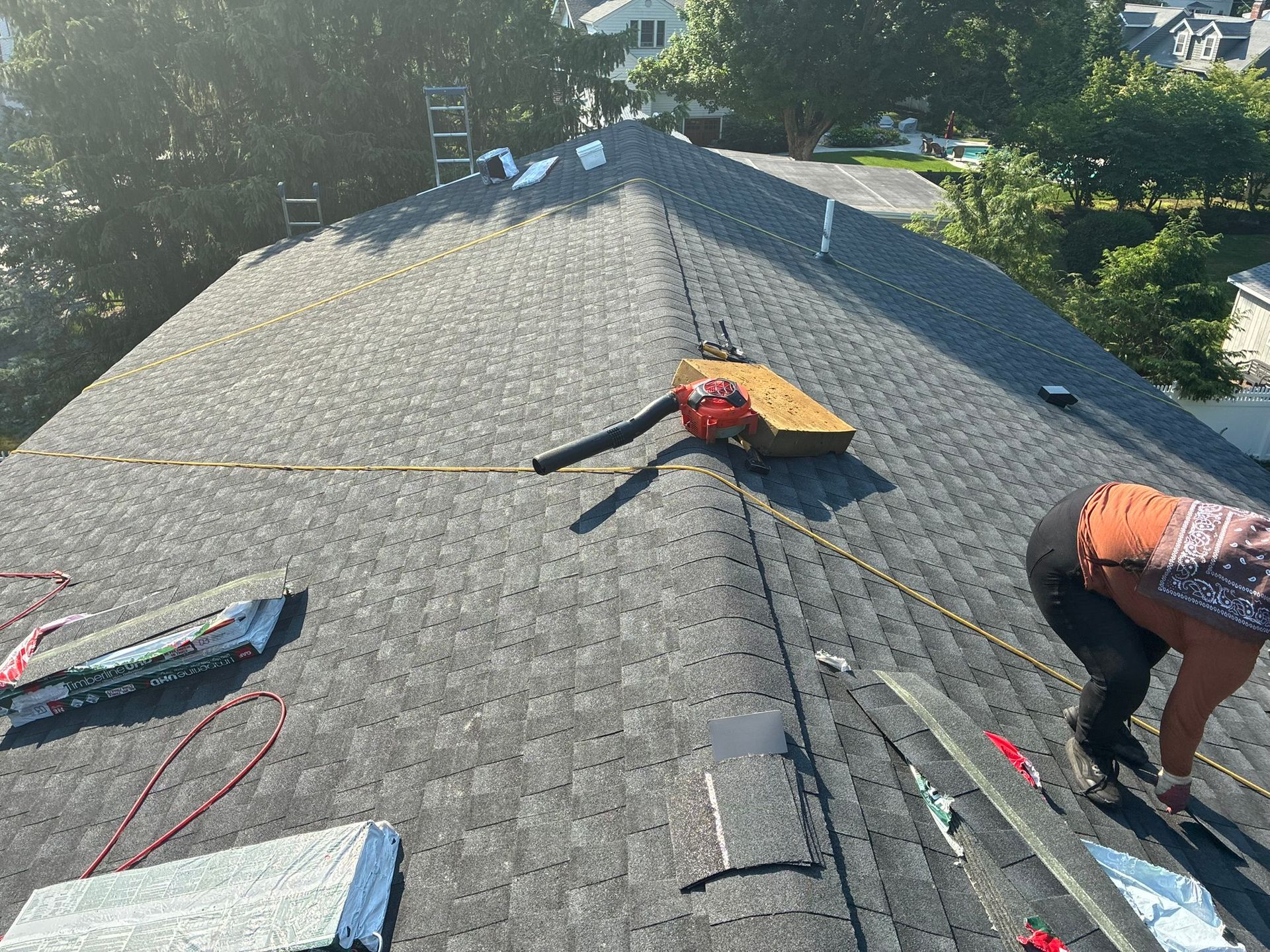 Roofers installing shingles on a gray roof, with tools and materials spread across the surface.