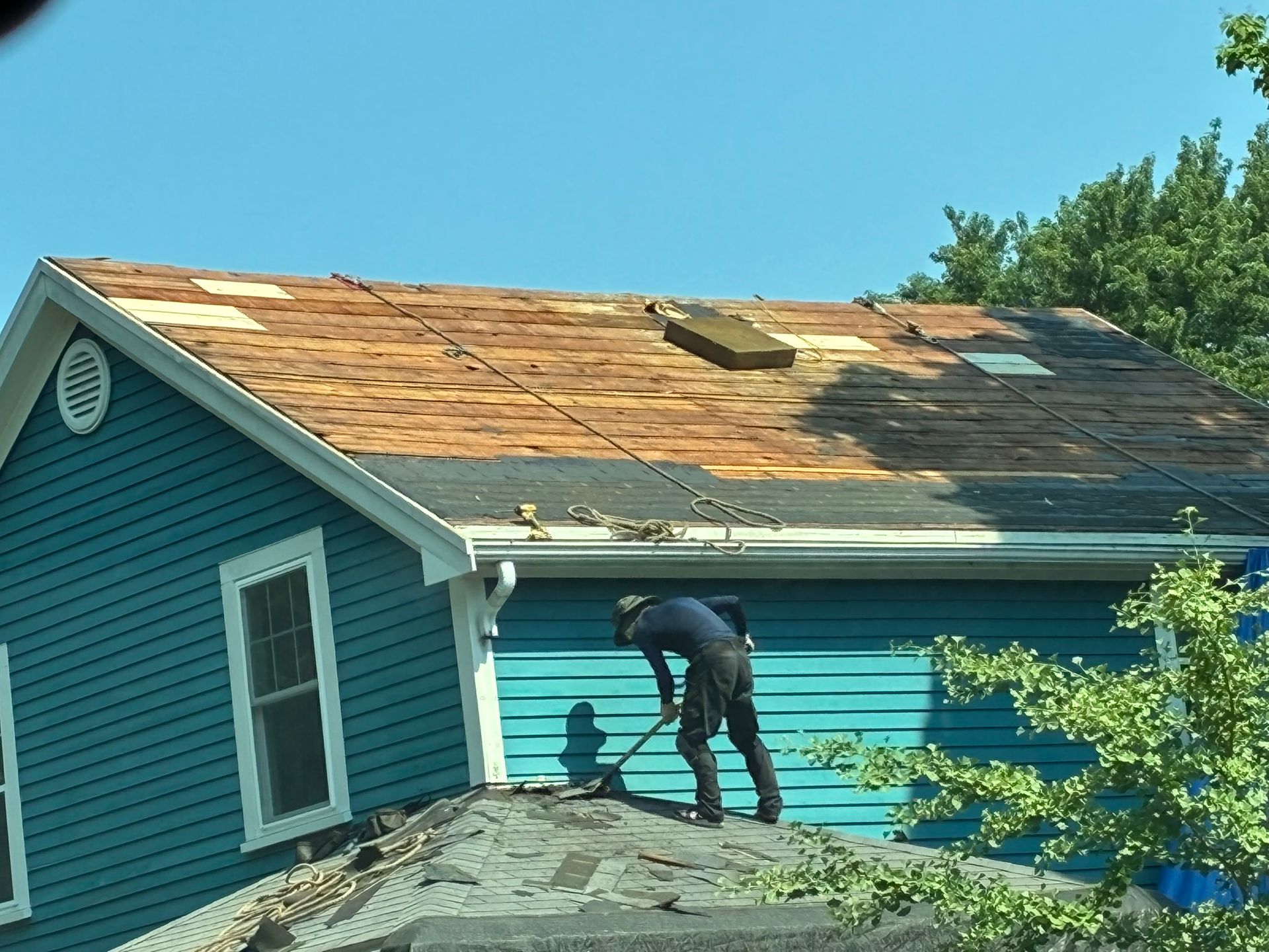 Person working on a blue house roof with damaged shingles