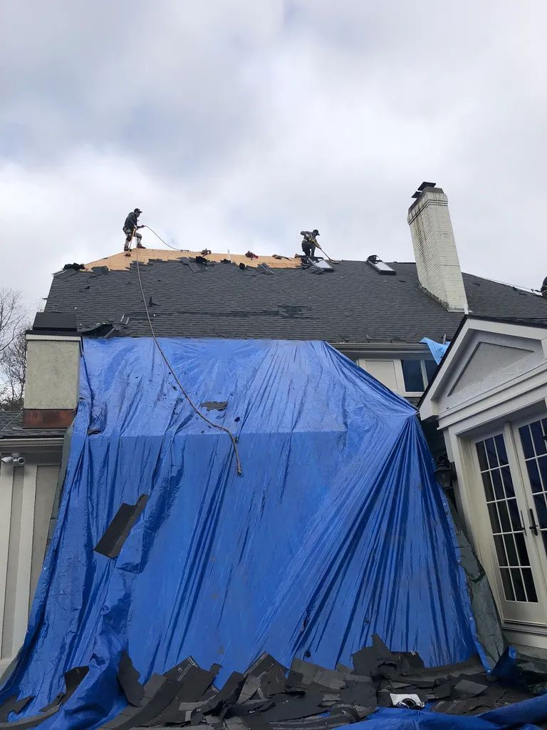 Blue tarp covering roof during repair, with workers on top and a cloudy sky above