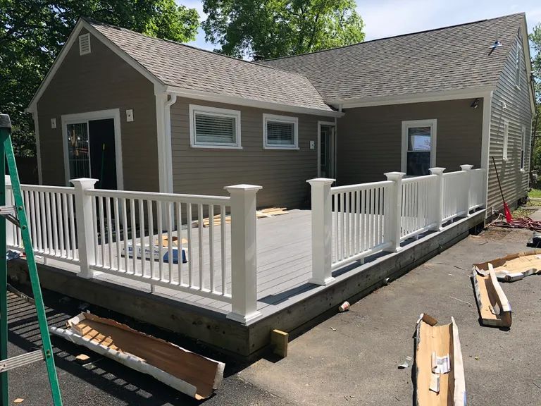 Gray house with a large raised wooden deck and white railings under construction