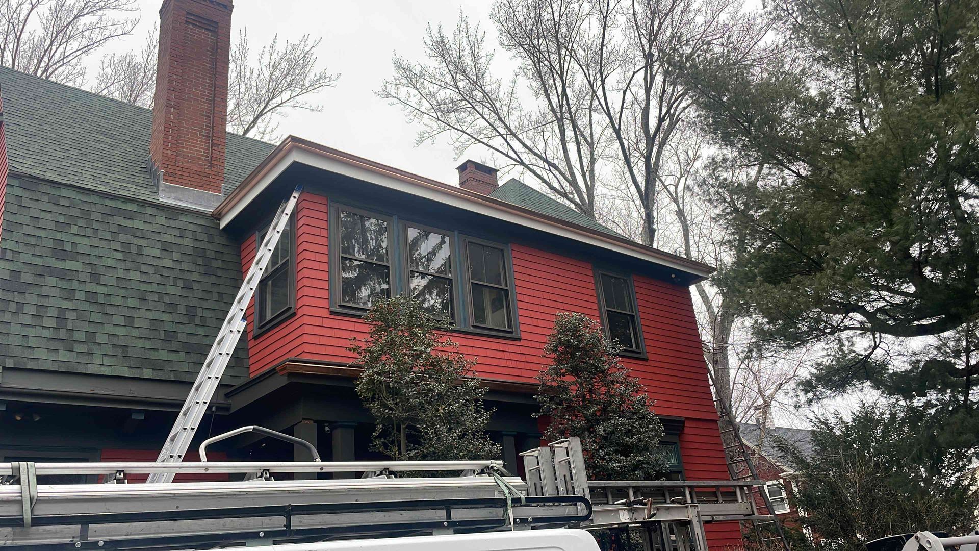 Red house with chimney, dark roof, and white-trimmed windows partly covered in snow