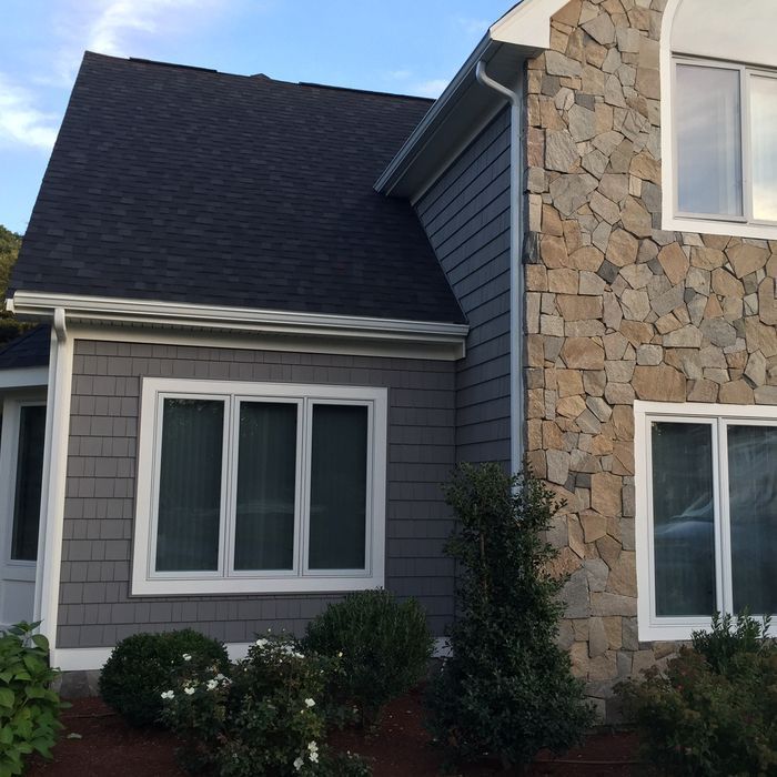 House exterior with gray siding, stone facade, white-trimmed windows, and shrubs in front yard