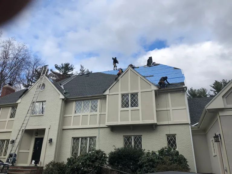 House roof under repair with blue tarp covering storm damage, under a cloudy sky
