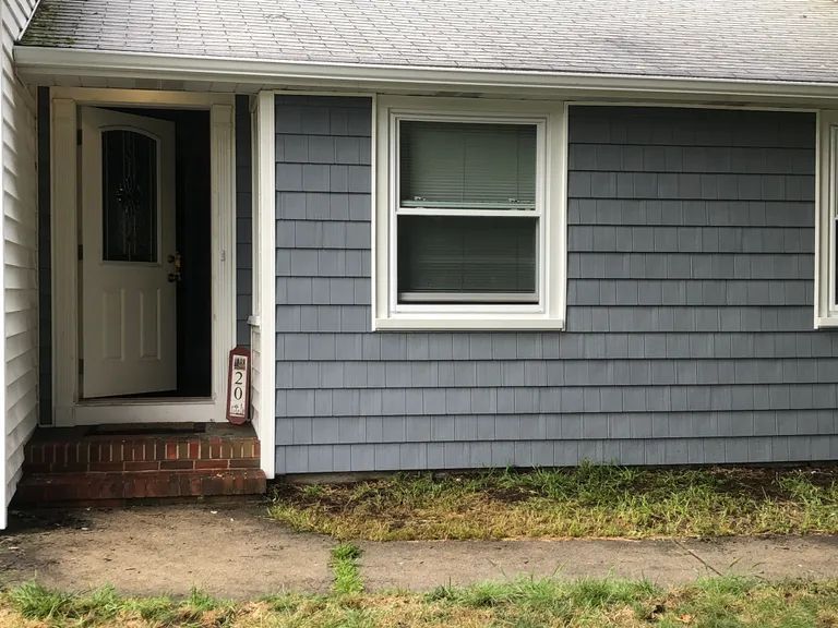 Front porch entrance of a gray house with white trim, small brick steps, and a window beside the door.