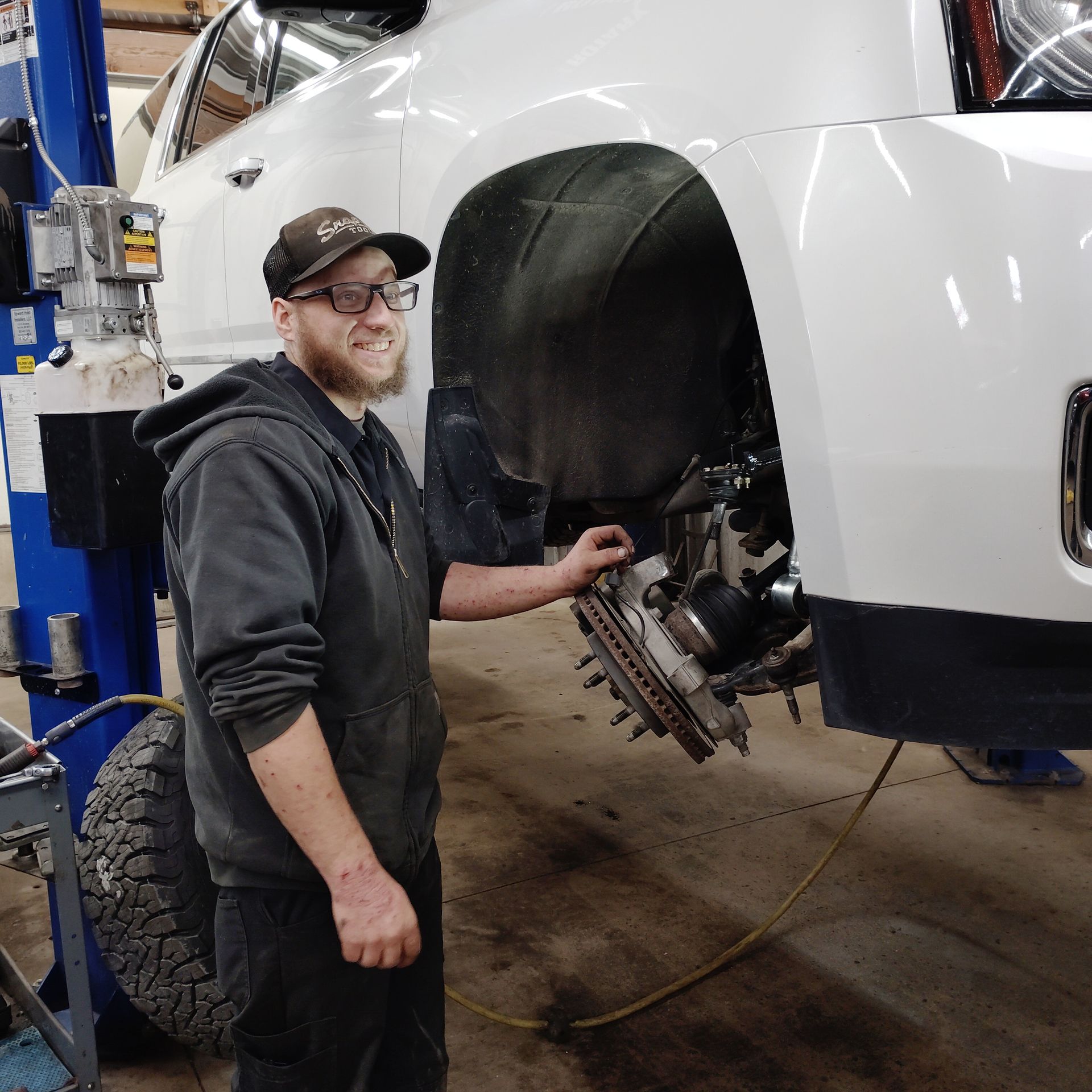 Mechanic smiling beside a car with the wheel removed in an auto repair shop