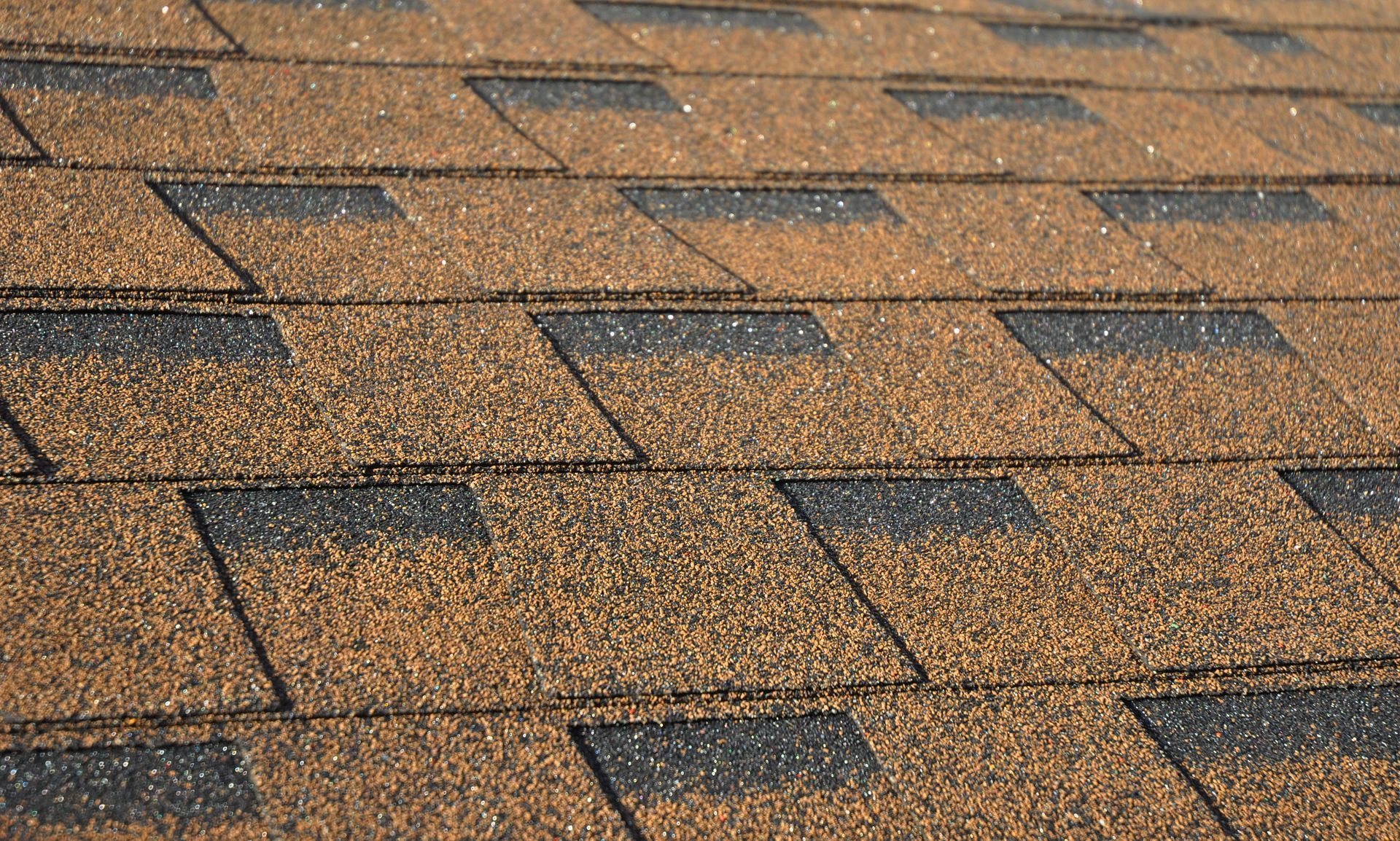 Close-up of a brown shingled roof with dark rectangular patches and sunlit texture.