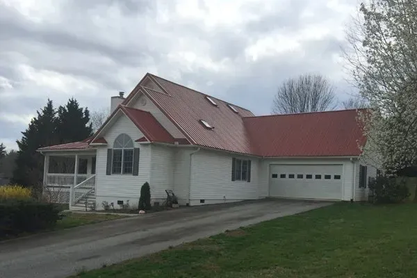 White house with red roof and attached garage on a cloudy day, viewed from the driveway.