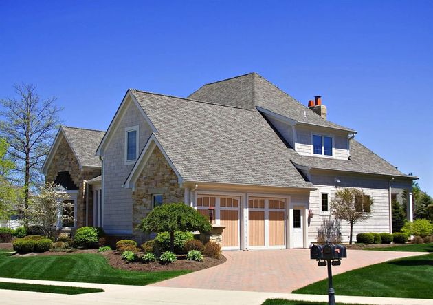Suburban house with gray shingled roof, beige siding, manicured lawn, and blue sky