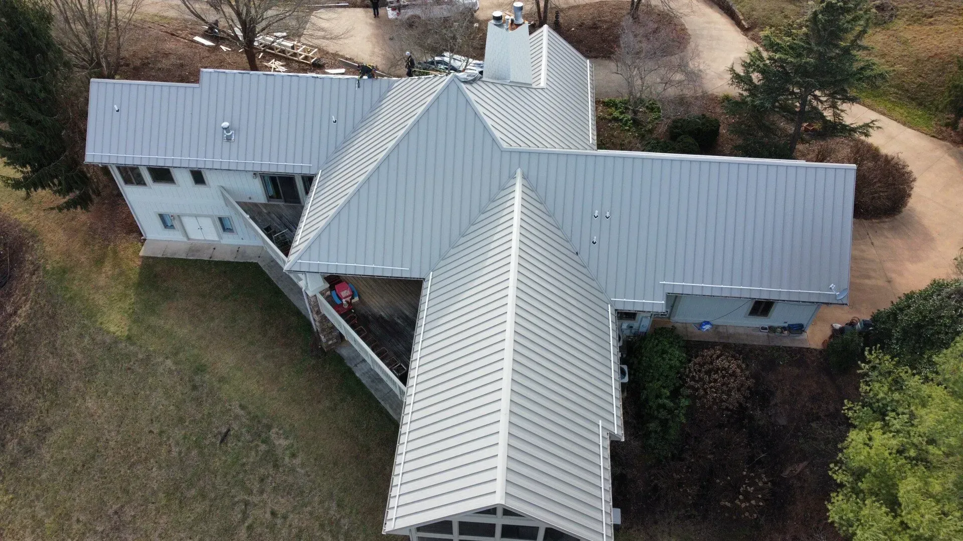 Aerial view of a house with a gray metal roof and covered front porch, surrounded by trees and lawn
