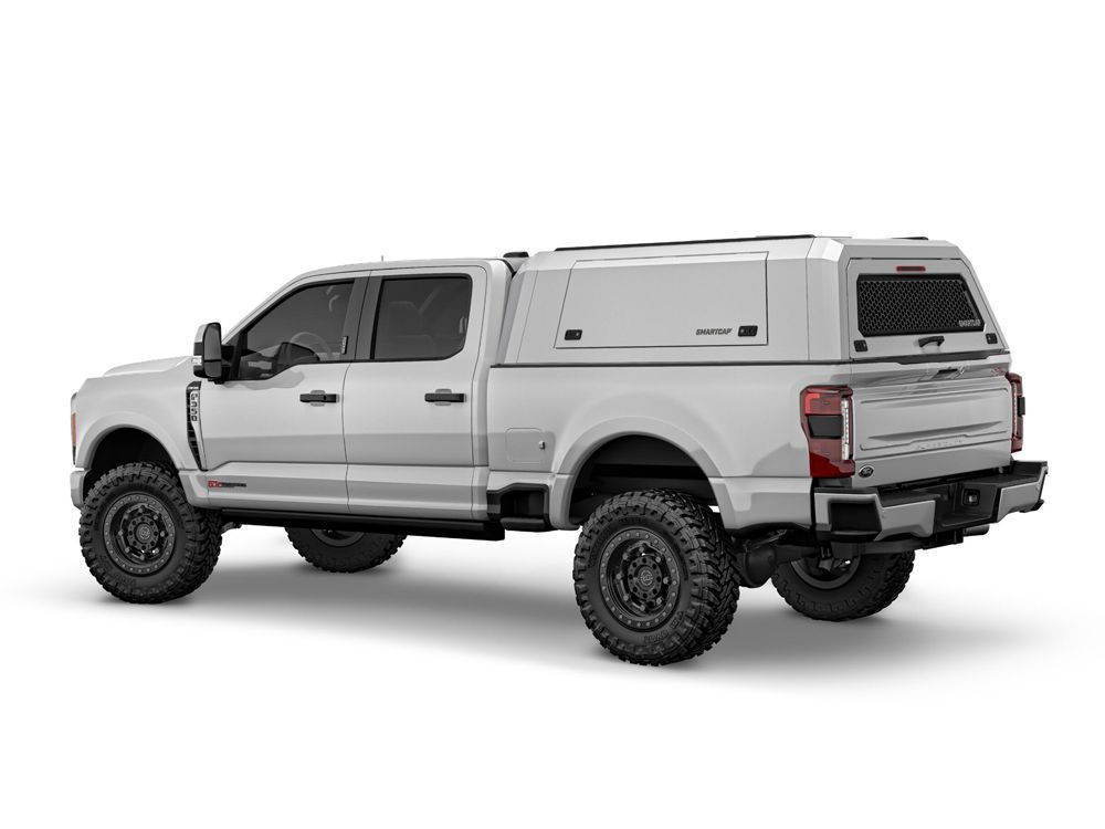 Silver pickup truck with a camper shell, black wheels, and lifted suspension.