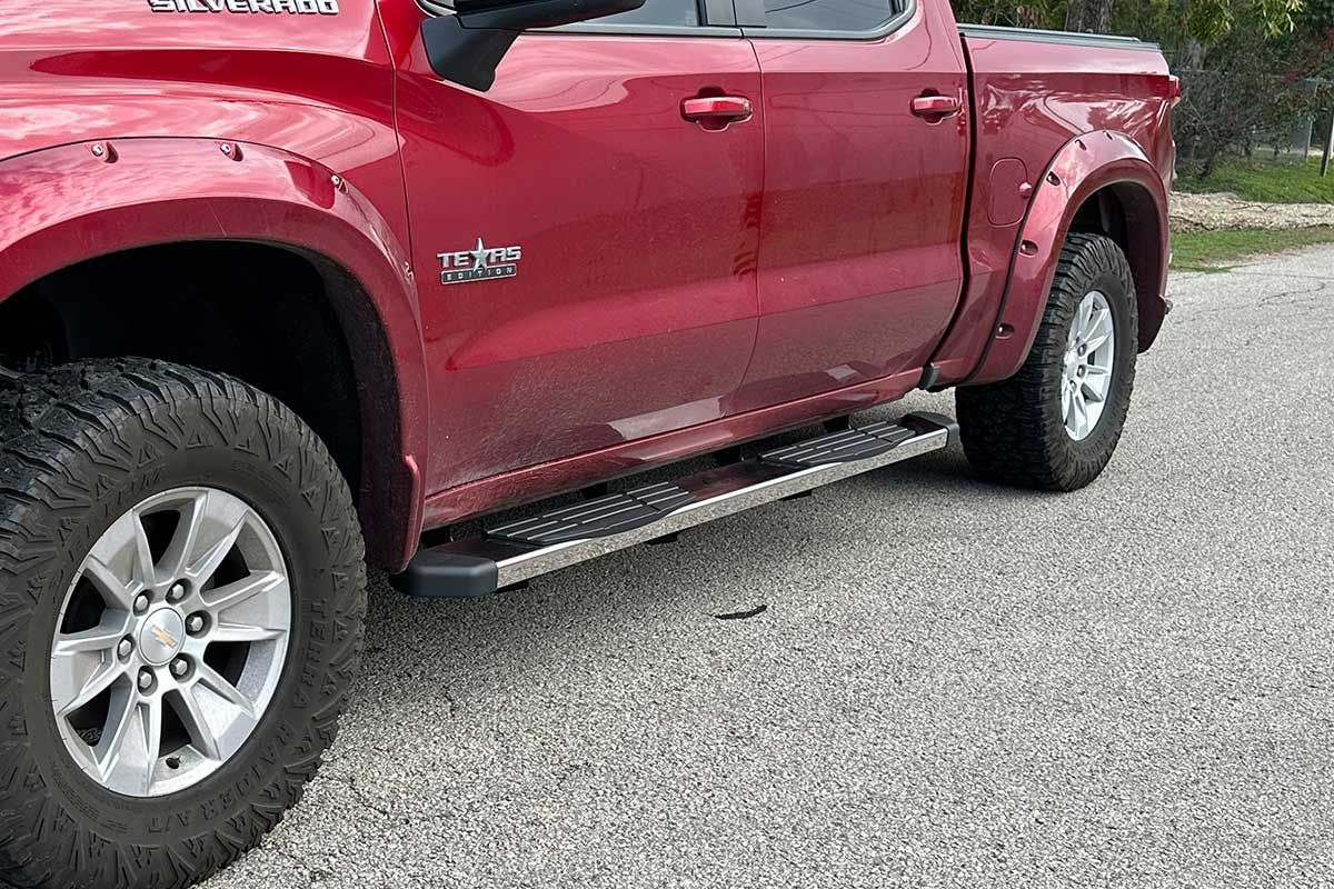 red Chevy pickup truck with black tires and chrome side steps
