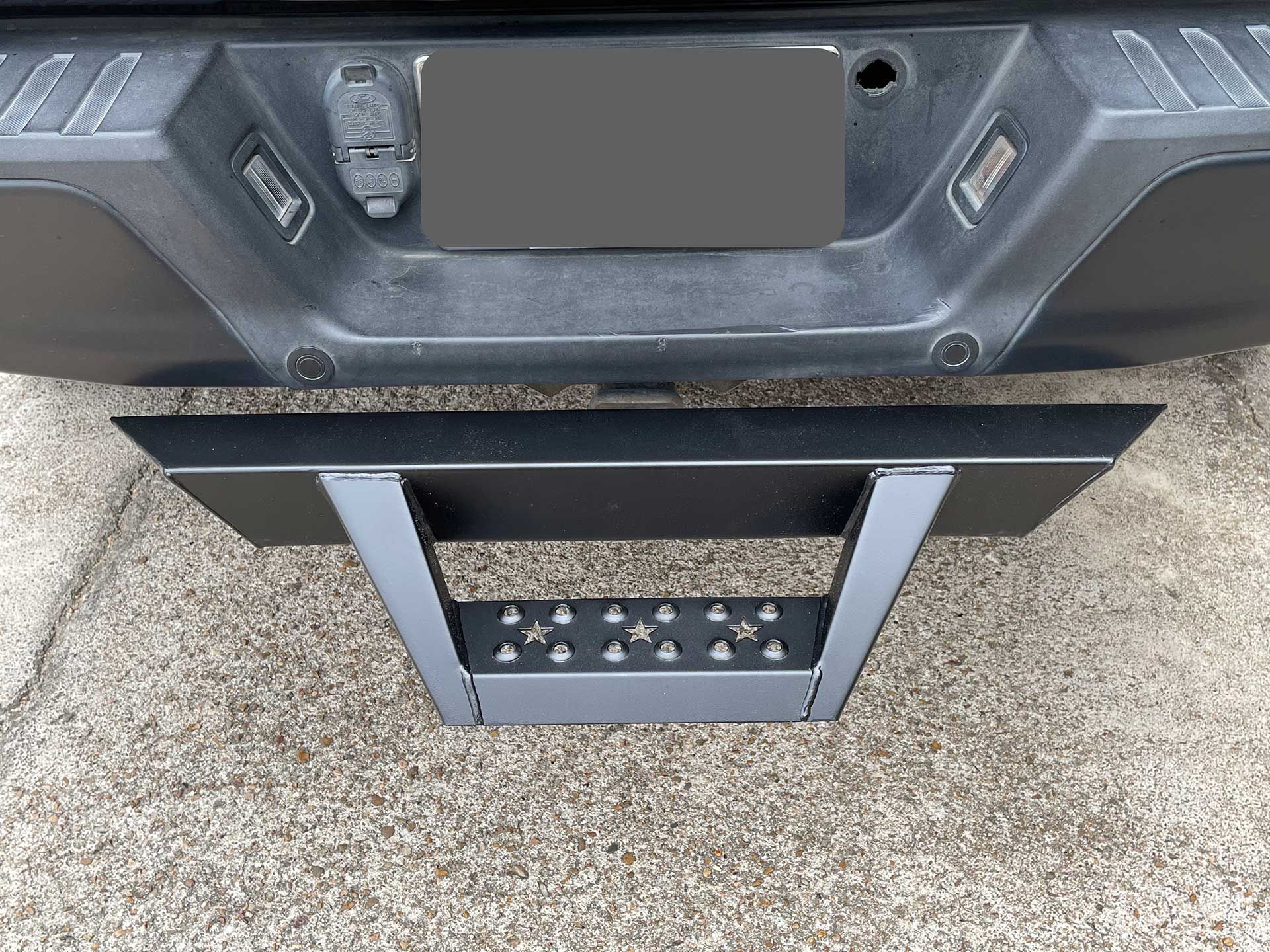 black truck bumper with a black step attachment lying on the ground below it