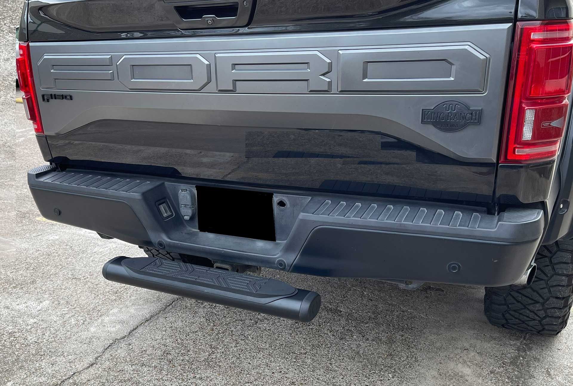 black Ford Raptor truck rear bumper with step, license plate obscured