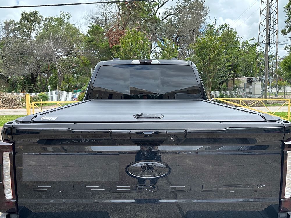 Rear view of a black pickup truck with a closed bed cover, parked outside.