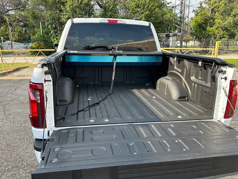 White pickup truck bed, open tailgate, black bed liner, blue tonneau cover.