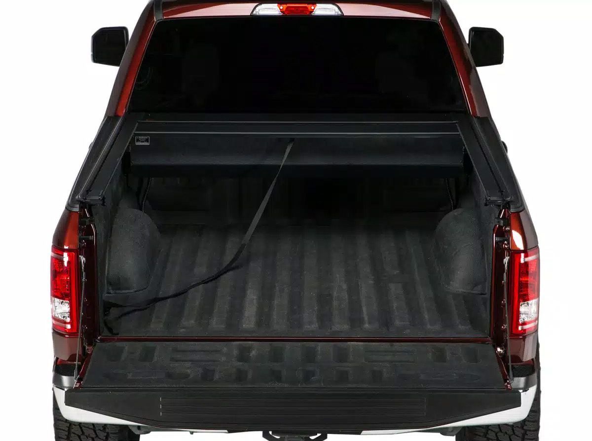 Red pickup truck bed open, black tonneau cover rolled back, showing bed liner.