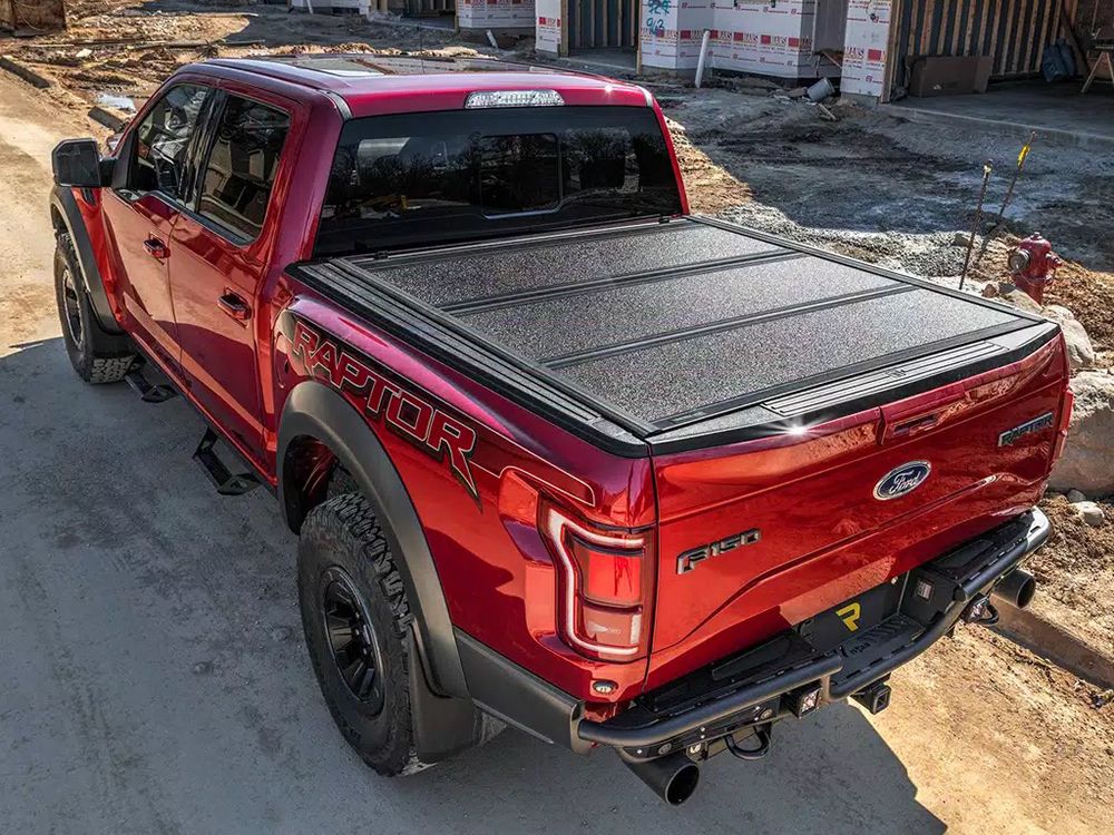 Red Ford Raptor truck with black bed cover parked near a construction site.