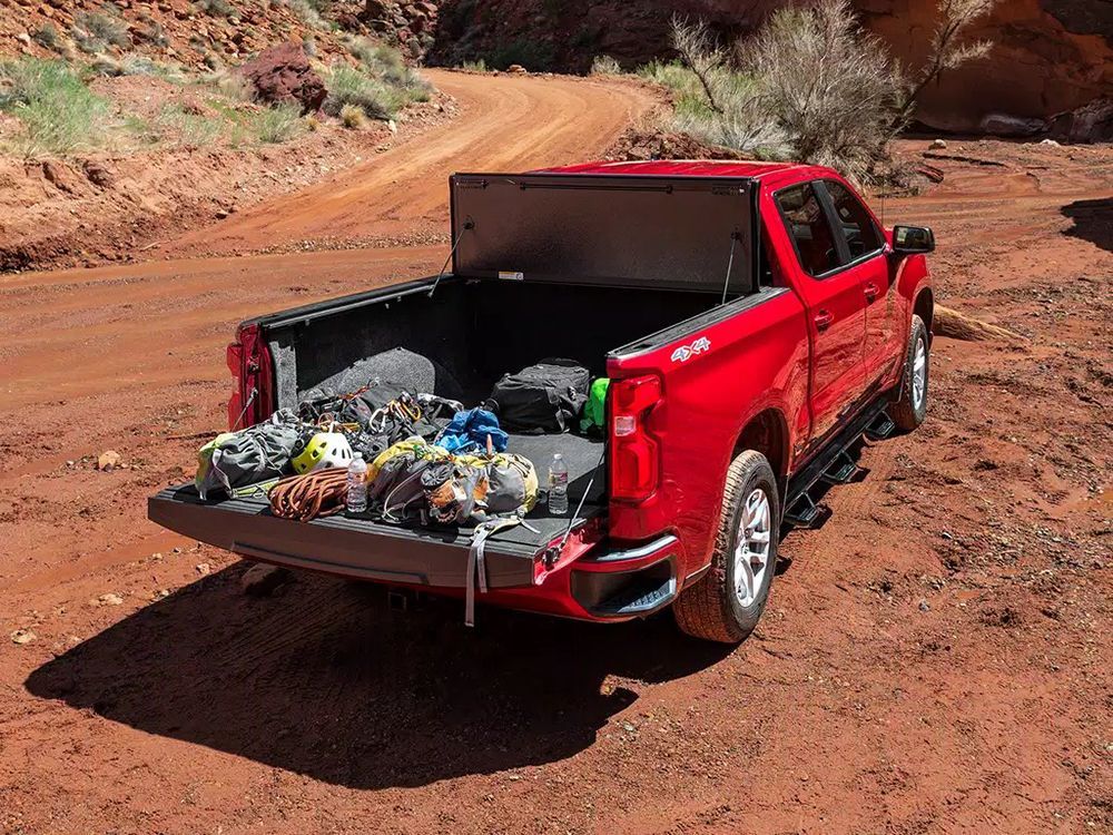 Red pickup truck with open tailgate, filled with climbing gear, on a dirt road in a canyon.