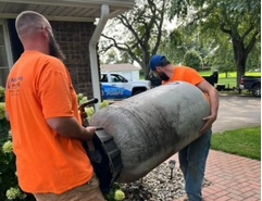 two men in orange shirts carrying a tank, residential well work
