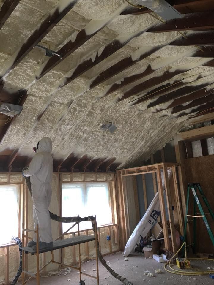 A man is spraying foam on the ceiling of a room.