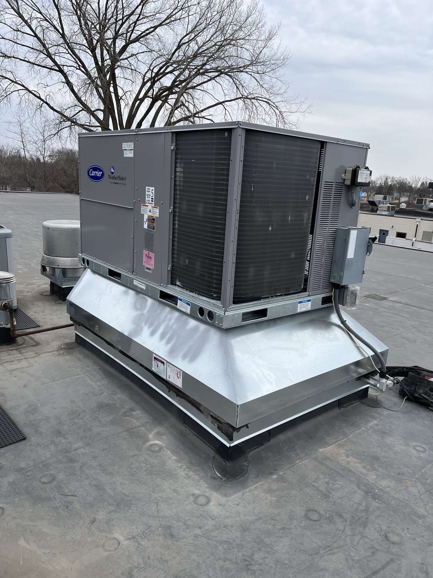 Rooftop HVAC unit, Carrier brand, gray and silver, on a commercial building roof.