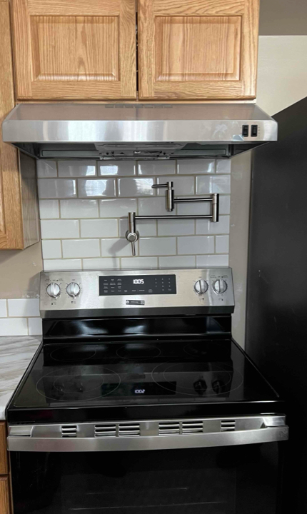 Stainless steel kitchen range and hood with tiled backsplash, wooden cabinets above.