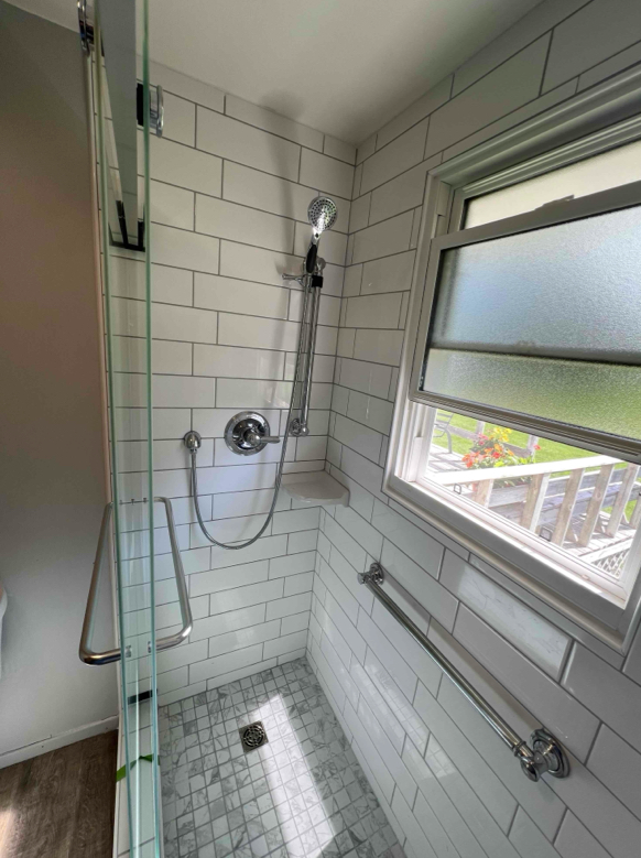 Shower stall with subway tile, glass door, and an open window.
