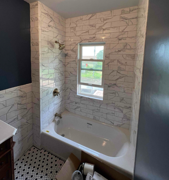 Bathroom with white subway tile, a window above the bathtub, and dark blue walls.
