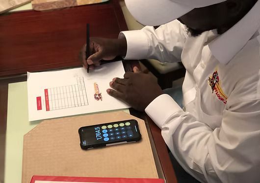 Person in a white shirt writing on a form at a desk with a smartphone nearby