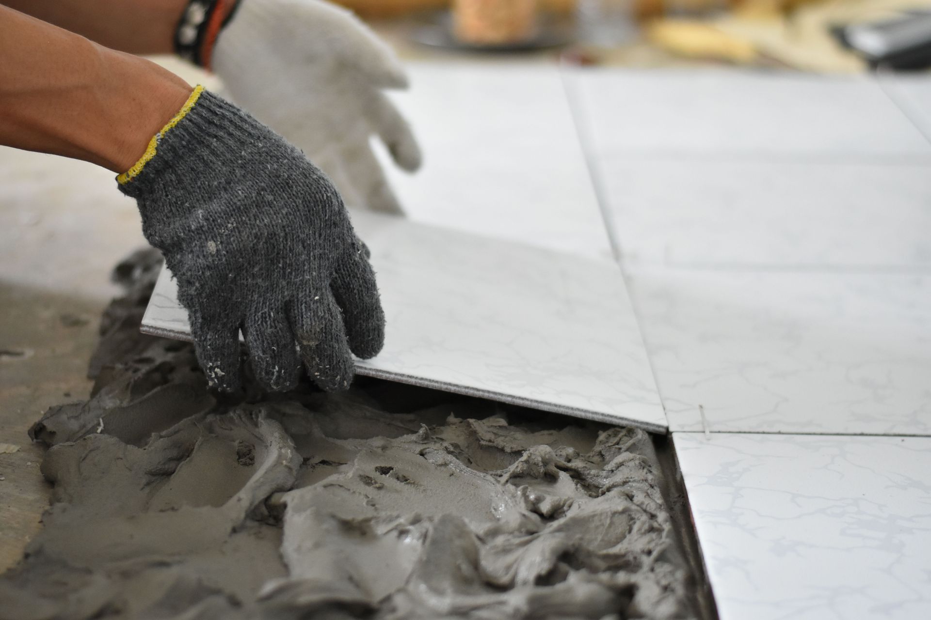 Gloved hand laying a gray tile into wet mortar during floor installation