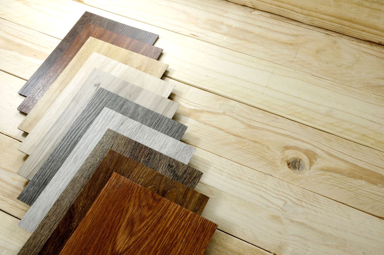 Stacked wood flooring samples in various shades on a light wooden surface
