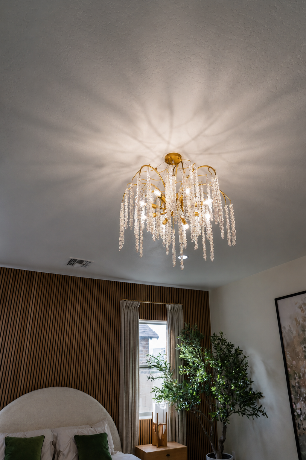 Crystal chandelier on a ceiling, casting light in a cozy living room with curtains, plant, and chair.