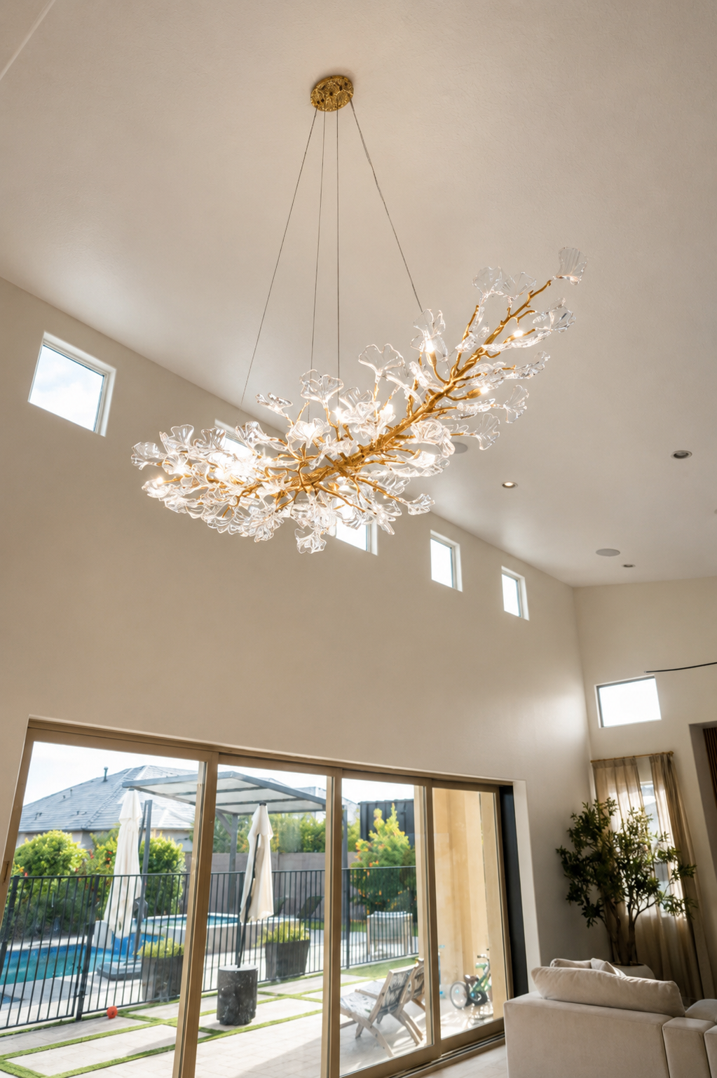 Modern living room with a large gold branch chandelier and tall windows overlooking a patio.