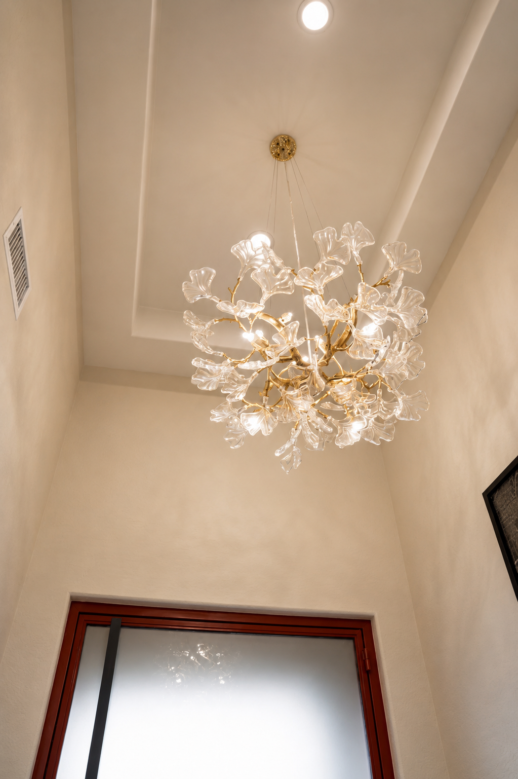 Elegant gold-and-white chandelier hanging from a high ceiling in a cream-colored hallway