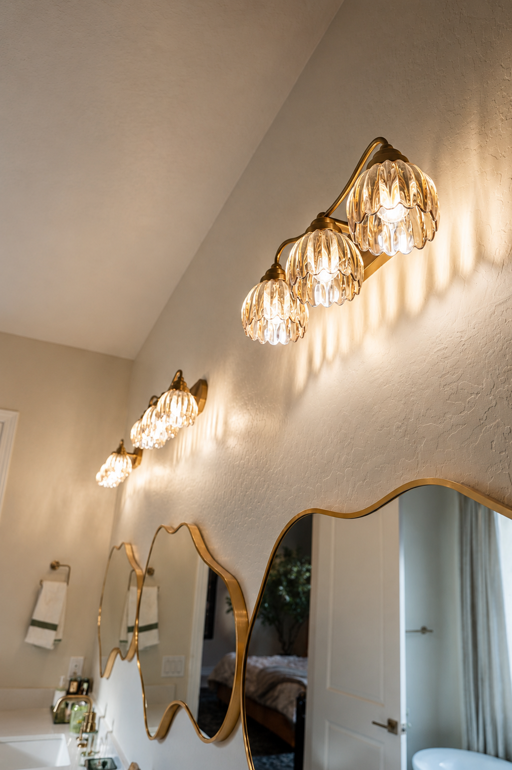 Bathroom wall with wavy mirror and gold sconces above a white sink cabinet